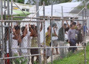Asylum seekers stand behind a fence in Oscar compound at the Manus Island detention centre in Papua New Guinea, Friday, March 21, 2014. Papua New Guinea expects to start resettling refugees detained in Australia's offshore processing centre on Manus Island as early as May. (AAP Image/Eoin Blackwell) 